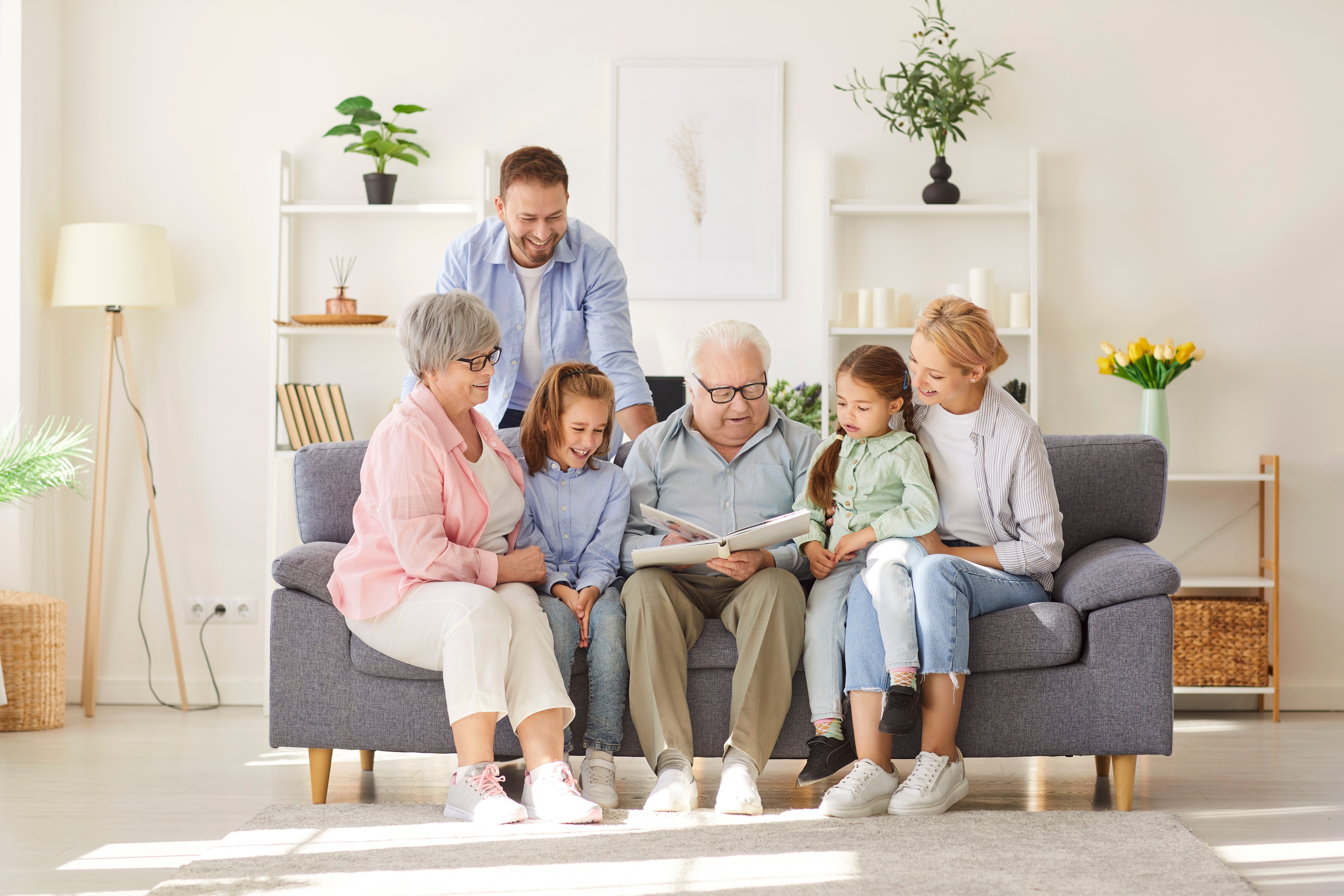 Rodina napříč generacemi sedí na pohovce a společně si prohlíží knihu.